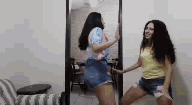 two women are dancing in front of a mirror in a living room .