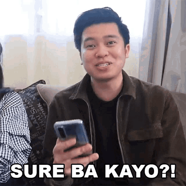 a man sitting on a couch holding a cell phone with the words sure ba kayo written below him