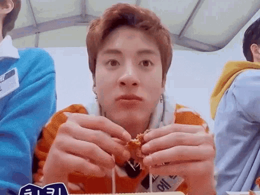 a young man is sitting at a table eating a chicken sandwich .