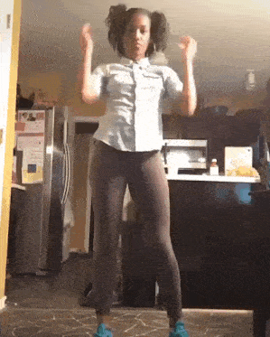 a woman is dancing in a kitchen in front of a refrigerator and microwave