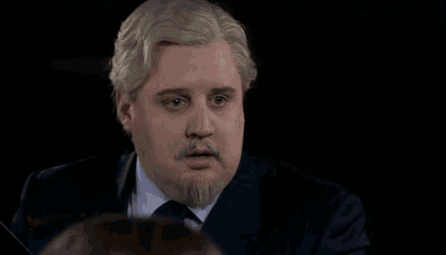 a man with gray hair and a beard is wearing a blue suit and tie