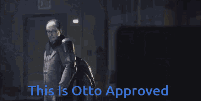 a man with glasses stands in front of a robotic arm that says this is otto approved