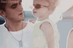 a man is holding a baby wearing sunglasses and a white shirt .