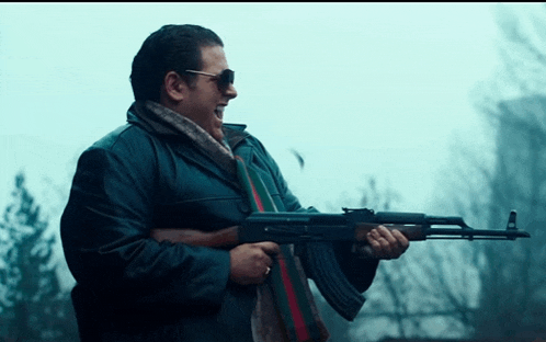 a man wearing sunglasses and a scarf is holding a rifle