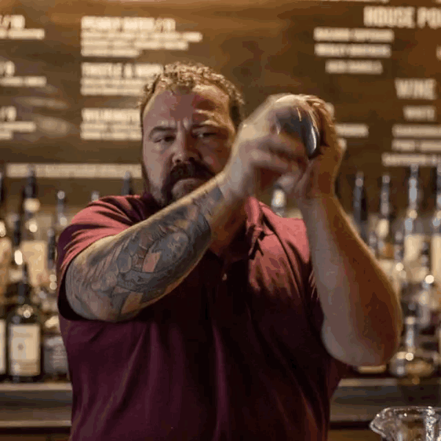 a man with a tattoo on his arm is shaking a drink in front of a blackboard that says house potion