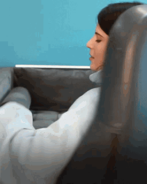 a woman sits on a couch with her eyes closed and a blue wall behind her