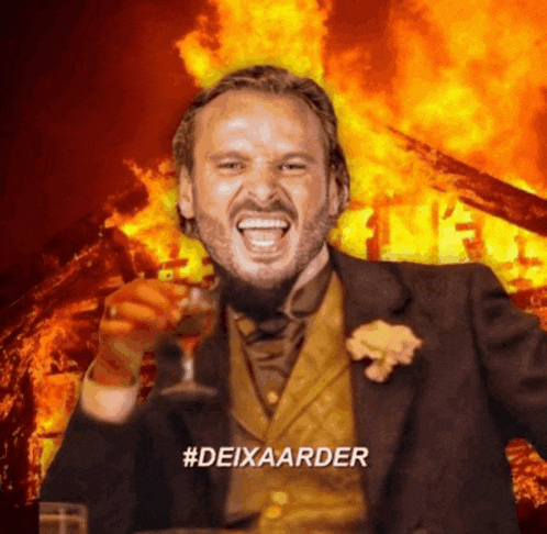 a man with a beard is holding a glass of wine in front of a burning building with the hashtag #deixaarder