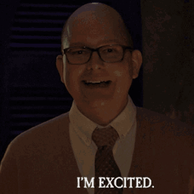 a bald man wearing glasses and a brown sweater says i 'm excited