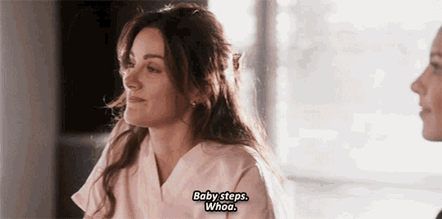 a woman in a pink scrub is talking to another woman and says baby steps whoa