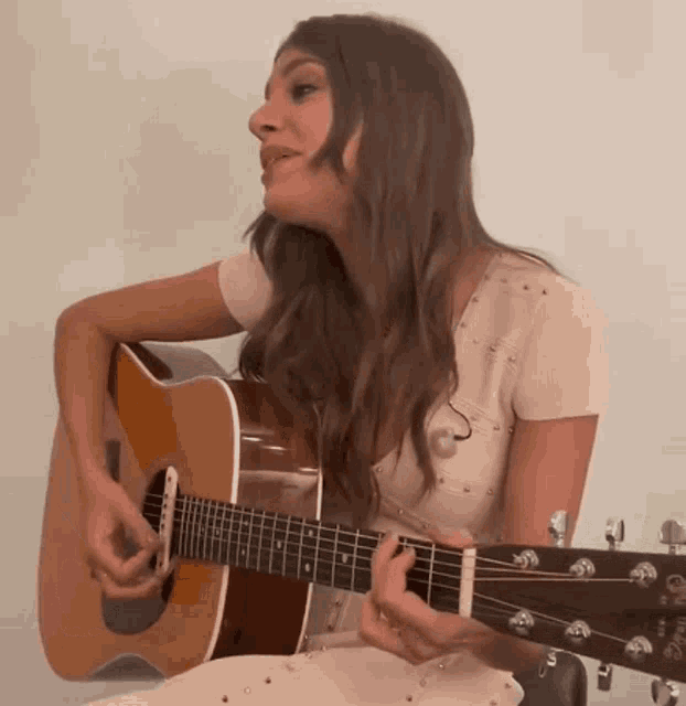 a woman in a white dress is playing an acoustic guitar and singing