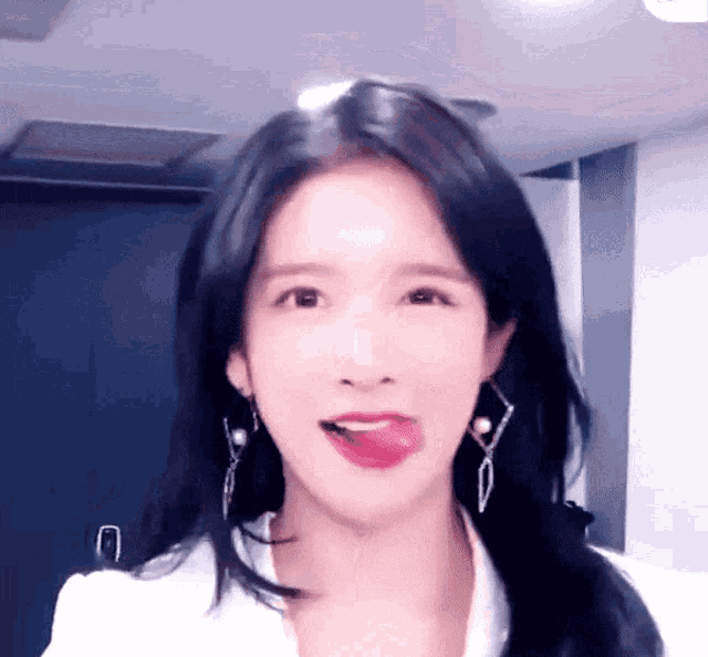 a woman wearing earrings and a white shirt is sticking out her tongue