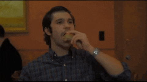 a man in a plaid shirt is eating a sandwich with a watch on his wrist