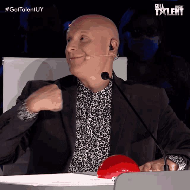 a bald man is sitting at a podium with a red button in front of him that says " got talent "
