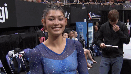 a woman in a blue leotard is smiling in front of a sign that says usa gymstore