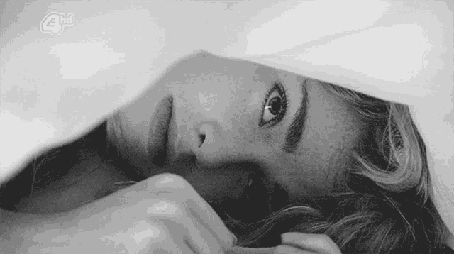 a black and white photo of a woman laying under a blanket with 4hd written on the bottom