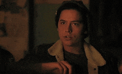 a young man wearing a denim jacket and a hat is sitting in a dark room .