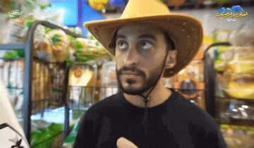 a man wearing a cowboy hat stands in front of a sign that says ' arabic '