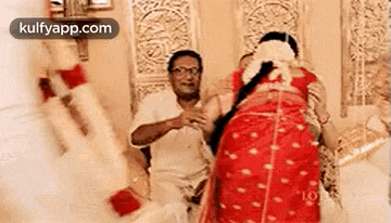 a man in a white shirt is sitting next to a woman in a red saree .
