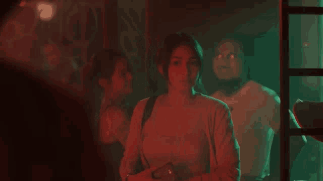 a woman is standing in a dark room with a red light on her face