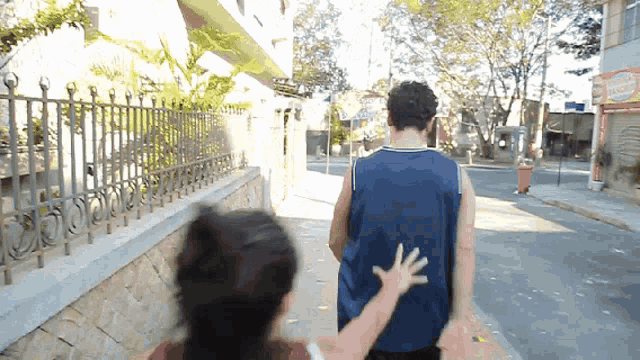 a man in a blue tank top is walking down a street with a woman holding his hand