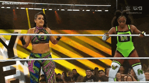 two female wrestlers are standing in a ring with a crowd watching .