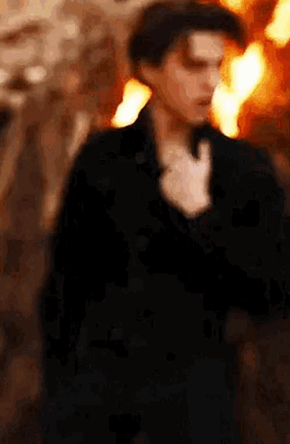 a blurry picture of a man standing in front of a fire with his hand on his chest .