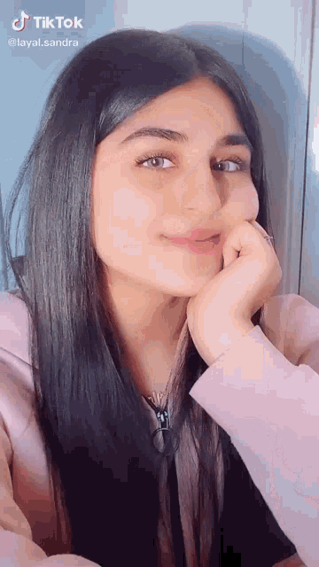 a girl with long black hair is looking at the camera with her hand on her face ..