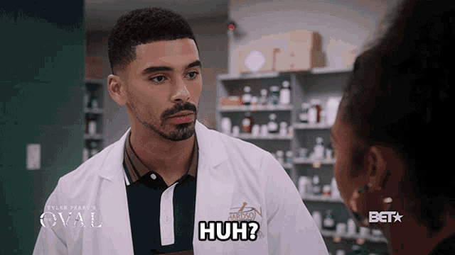 a man in a lab coat is talking to a woman in a pharmacy and says huh