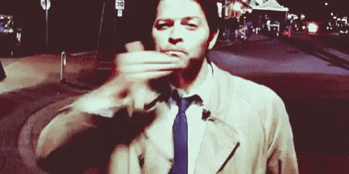 a man wearing a trench coat and tie is covering his mouth with his hand .