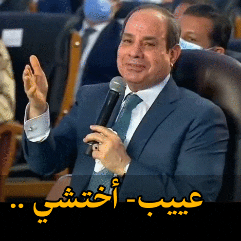 a man in a suit and tie is holding a microphone with arabic writing behind him
