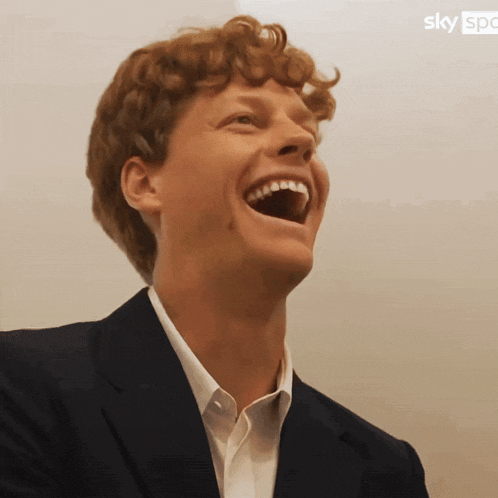 a man in a suit and white shirt is laughing in front of a sky logo