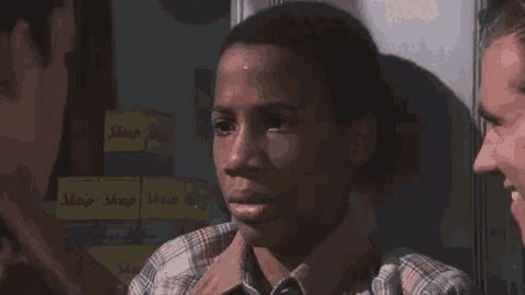 a boy in a plaid shirt is talking to two men in front of a stack of sharp sharp boxes .