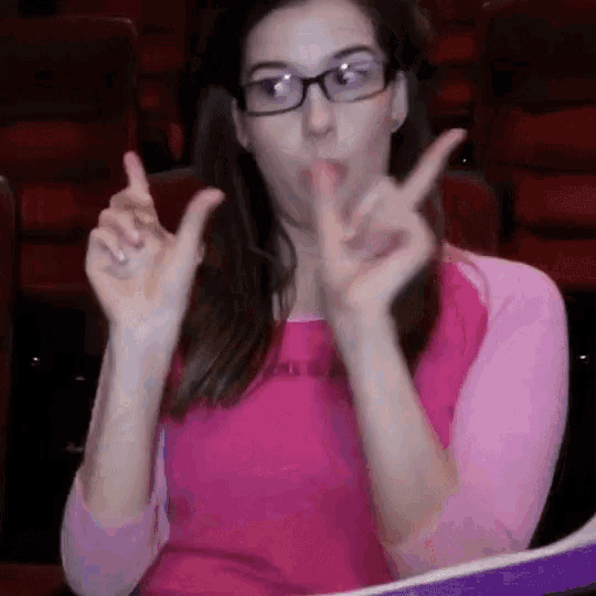 a woman wearing glasses and a pink shirt is making a peace sign with her hands
