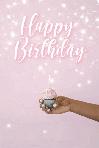 a hand is holding a cupcake with a lit candle in front of a sign that says happy birthday