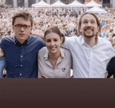 two men and a woman are posing for a picture in front of a crowd .