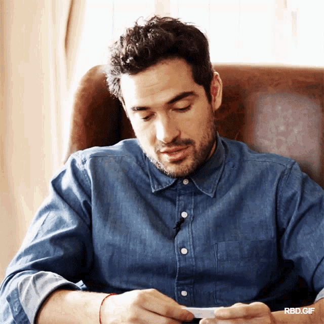 a man in a denim shirt is sitting in a chair looking down