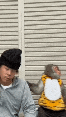 a man is sitting next to a stuffed monkey wearing a tiger costume and a hat .