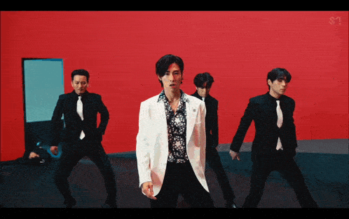 a group of men in suits and ties dancing in front of a red wall