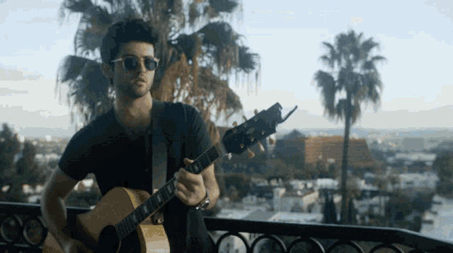 a man is playing a guitar on a balcony with palm trees in the background
