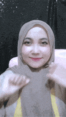 a woman wearing a hijab is smiling and making a peace sign with her hands .