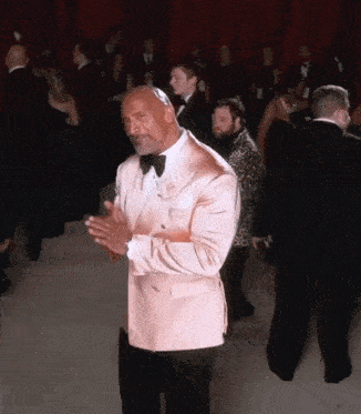 a man in a pink tuxedo and bow tie is clapping
