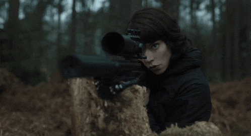 a woman in a black jacket holds a sniper rifle with a scope on her head