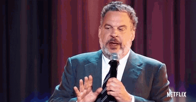 a man in a suit and tie is holding a microphone and talking into it .