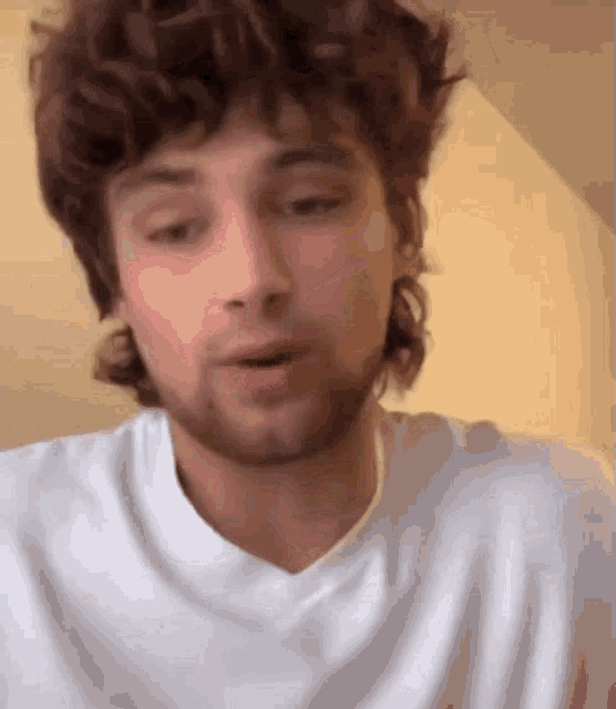 a man with curly hair and a beard is wearing a white shirt and looking at the camera .