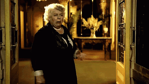 a woman in a black coat is standing in a hallway with a surprised look on her face