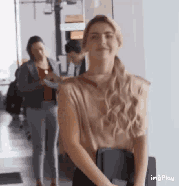 a woman is standing in a hallway with her hands behind her back and smiling .