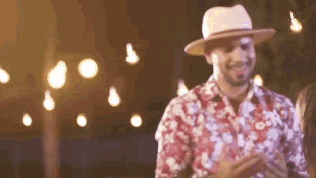 a man in a hat and floral shirt is dancing with a woman .