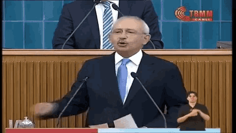 a man in a suit and tie is giving a speech in front of microphones with tbmm canli written on the bottom right