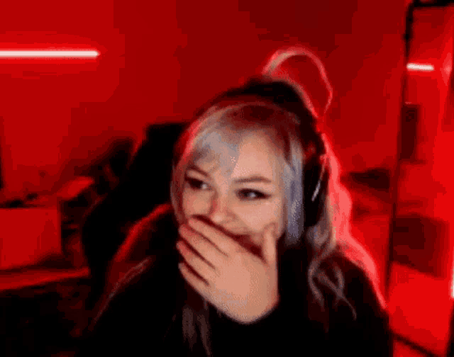 a woman wearing headphones is covering her mouth with her hand .