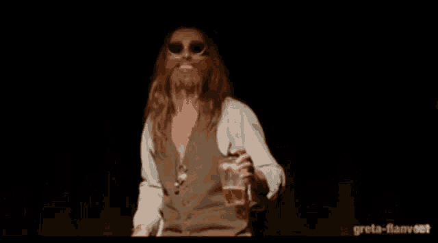 a man with a beard and sunglasses is holding a glass of beer ..
